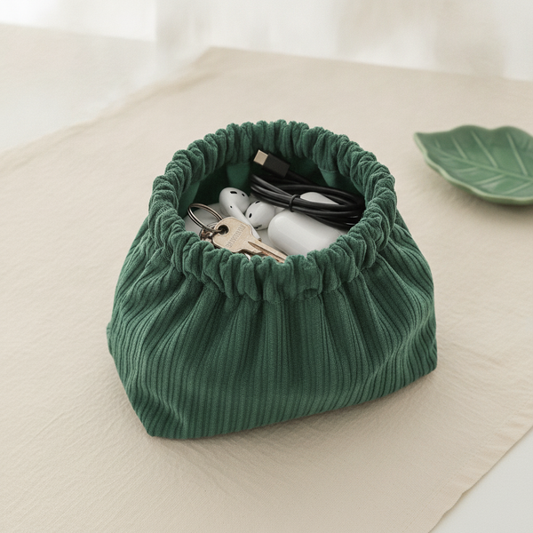 Close-up of a forest green corduroy elastic storage bag, filled with keys and earbuds, demonstrating the strong, secure elast